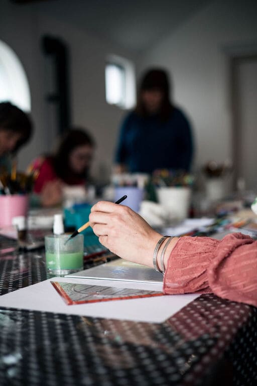 main qui peind et en arrière plan un groupe de personne qui font aussi de la peinture et dessin en art thérapie