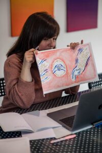 Thérèse-Marie Rossi qui montre un dessin à un ordinateur pour une personne qu'elle suit en art thérapie à distance