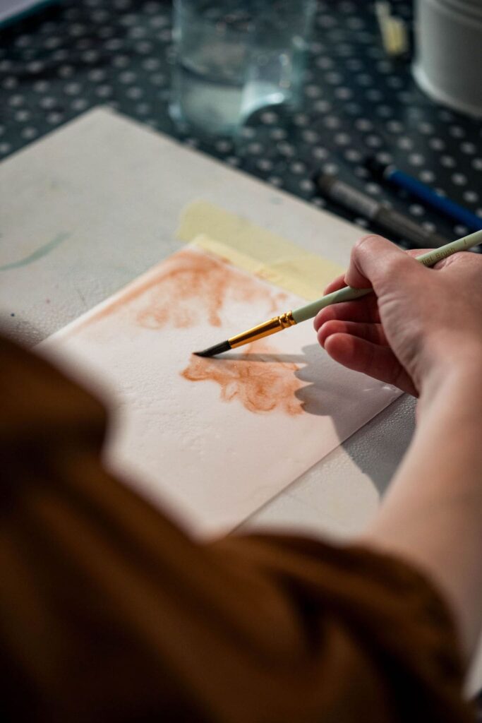 une main qui tient un pinceau et peind avec de l'aquarelle sur papier